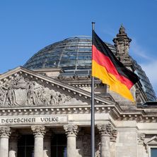 Deutscher Bundestag mit Kuppel davor eine wehende Deutschlandfahne
